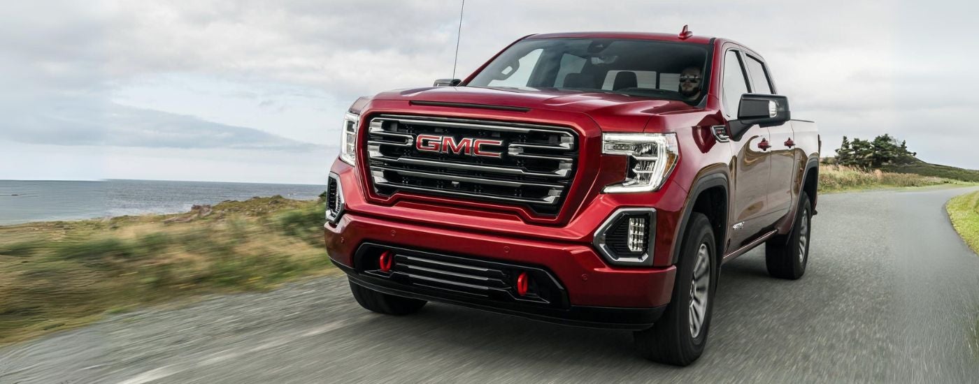 A red 2019 GMC Sierra 1500 AT4 is shown driving past a lake after leaving a GMC dealer.