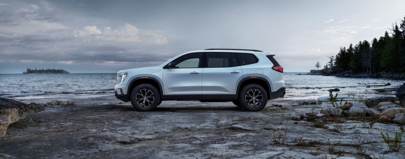 A white 2024 GMC Acadia AT4 is shown from the side next to a lake.