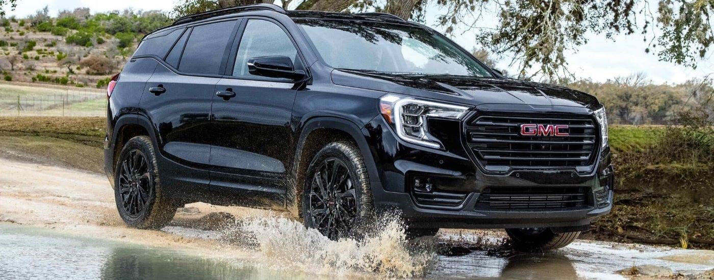 A black 2023 GMC Terrain for sale is shown driving off-road.